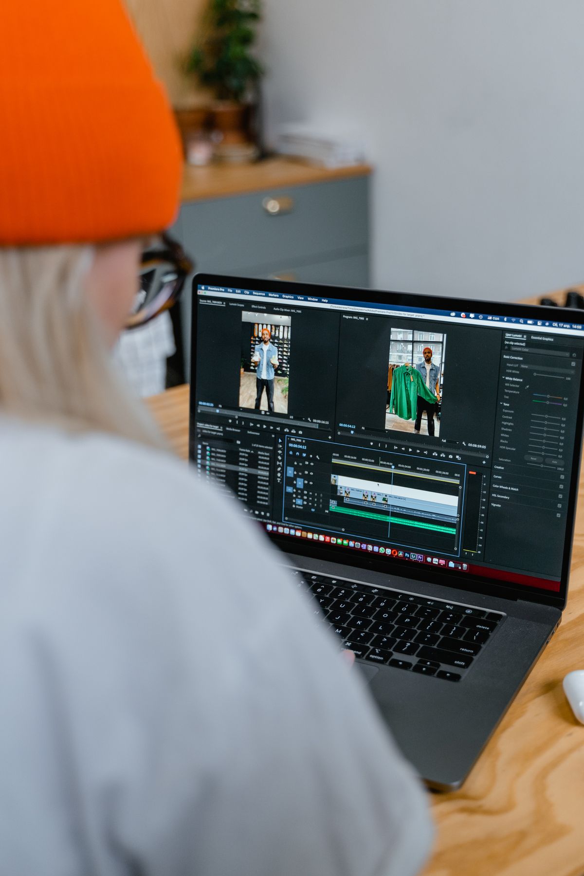 Perempuan bertopi oranye sedang mengedit video di laptop, layar menampilkan pratinjau video dan timeline editing