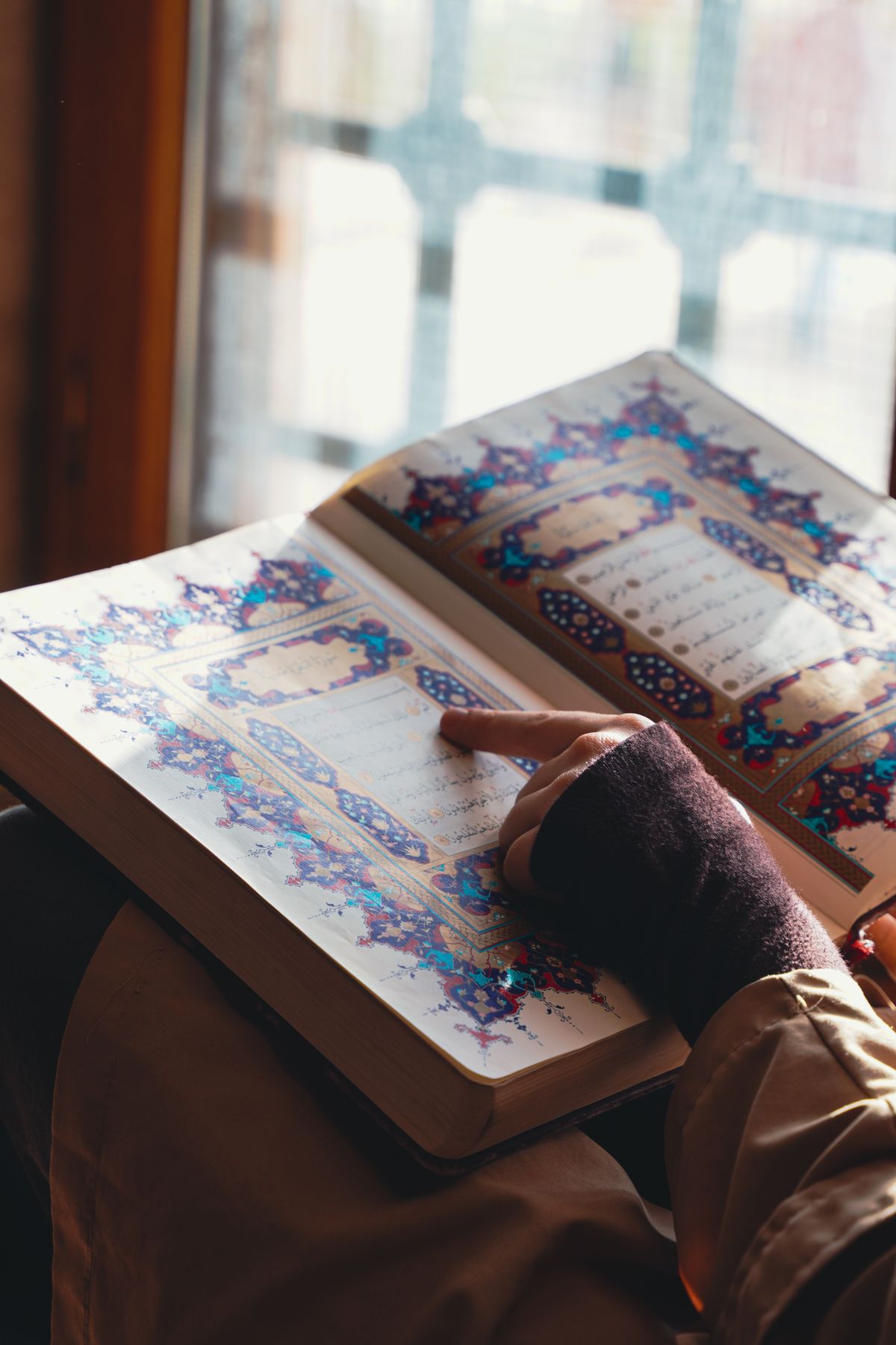 Seseorang membaca Al Quran dengan ornamen warna warni di dekat jendela, menggambarkan santri yang sedang mengaji