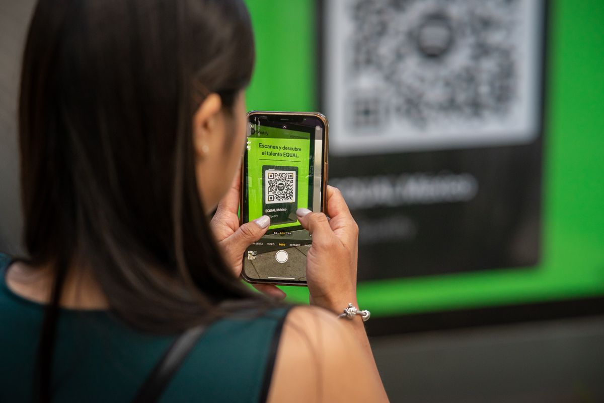 Seorang perempuan memindai kode QR dengan kamera ponselnya, menggambarkan cara memeriksa hasil kode QR sebelum disebar