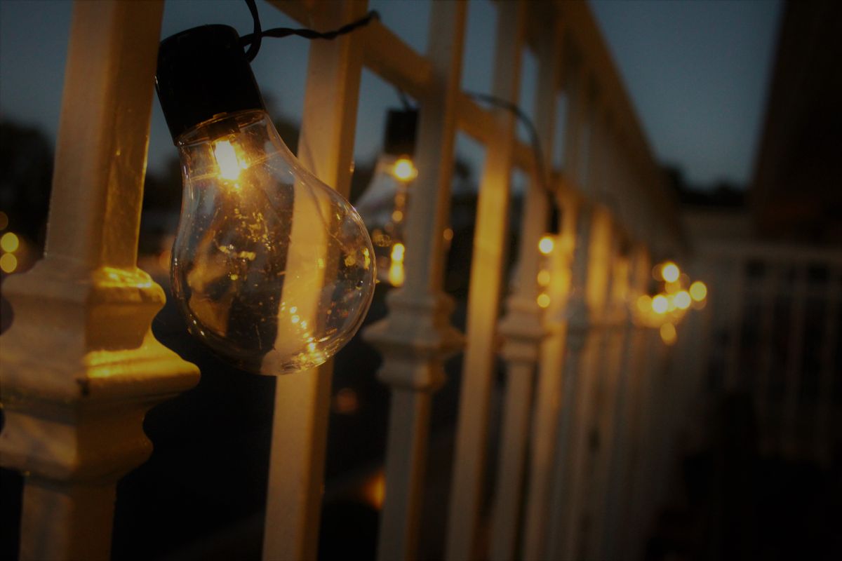 Rangkaian lampu bohlam yang menyala hangat di teras rumah saat senja, menggambarkan pemakaian listrik di rumah