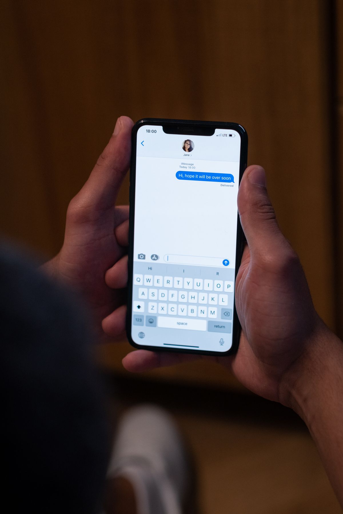 Tangan seseorang memegang HP dan mengetik pesan di aplikasi chat dengan papan ketik di layar