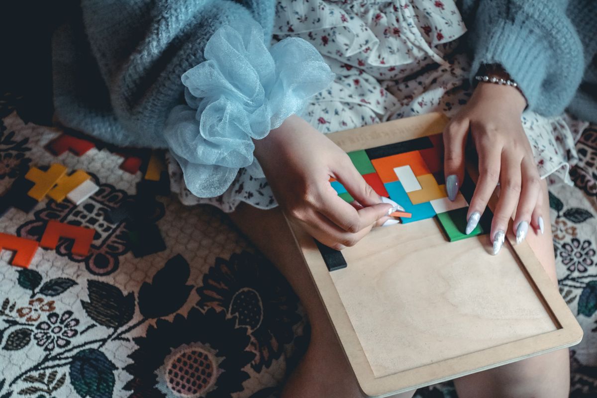 Seorang perempuan sedang menyusun potongan puzzle balok warna-warni di atas papan kayu, menggambarkan menyusun balok dengan teliti supaya papan tidak cepat penuh