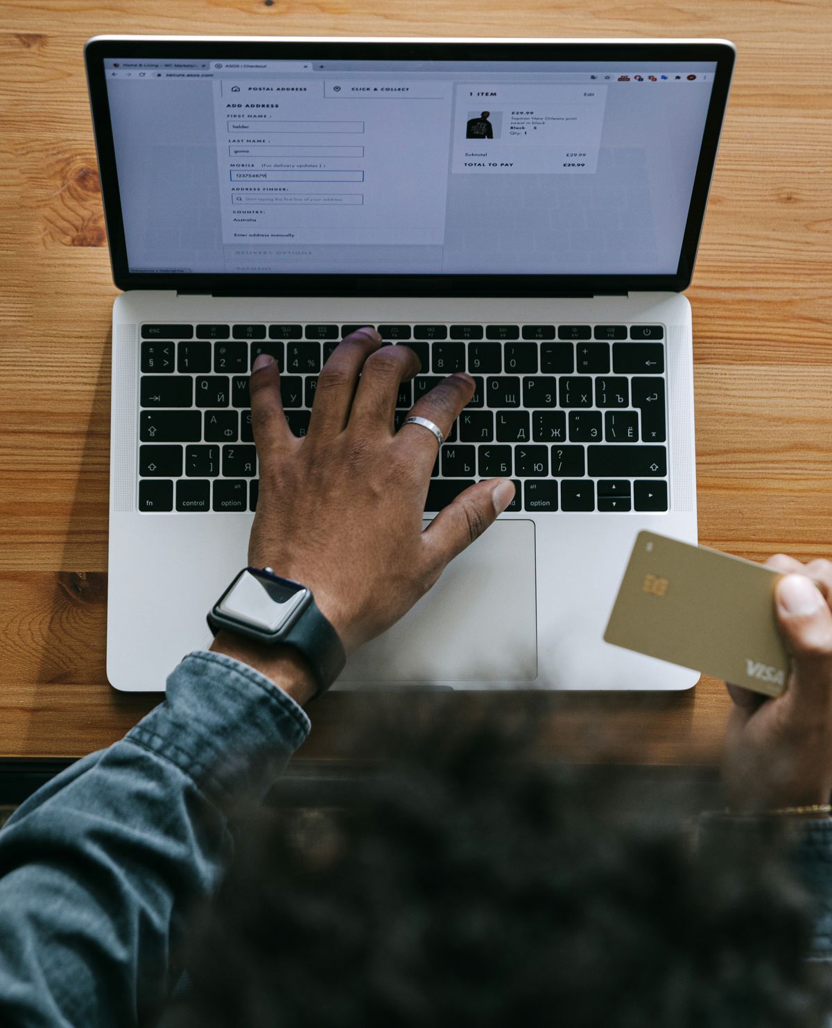 Tangan seseorang sedang membayar lewat laptop sambil memegang kartu, menggambarkan pembayaran biaya tambah daya secara online