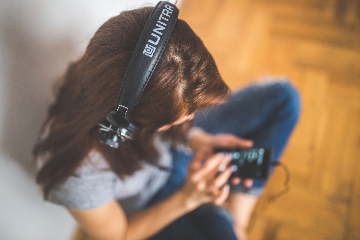 Perempuan memakai headphone sambil memegang HP, dilihat dari atas