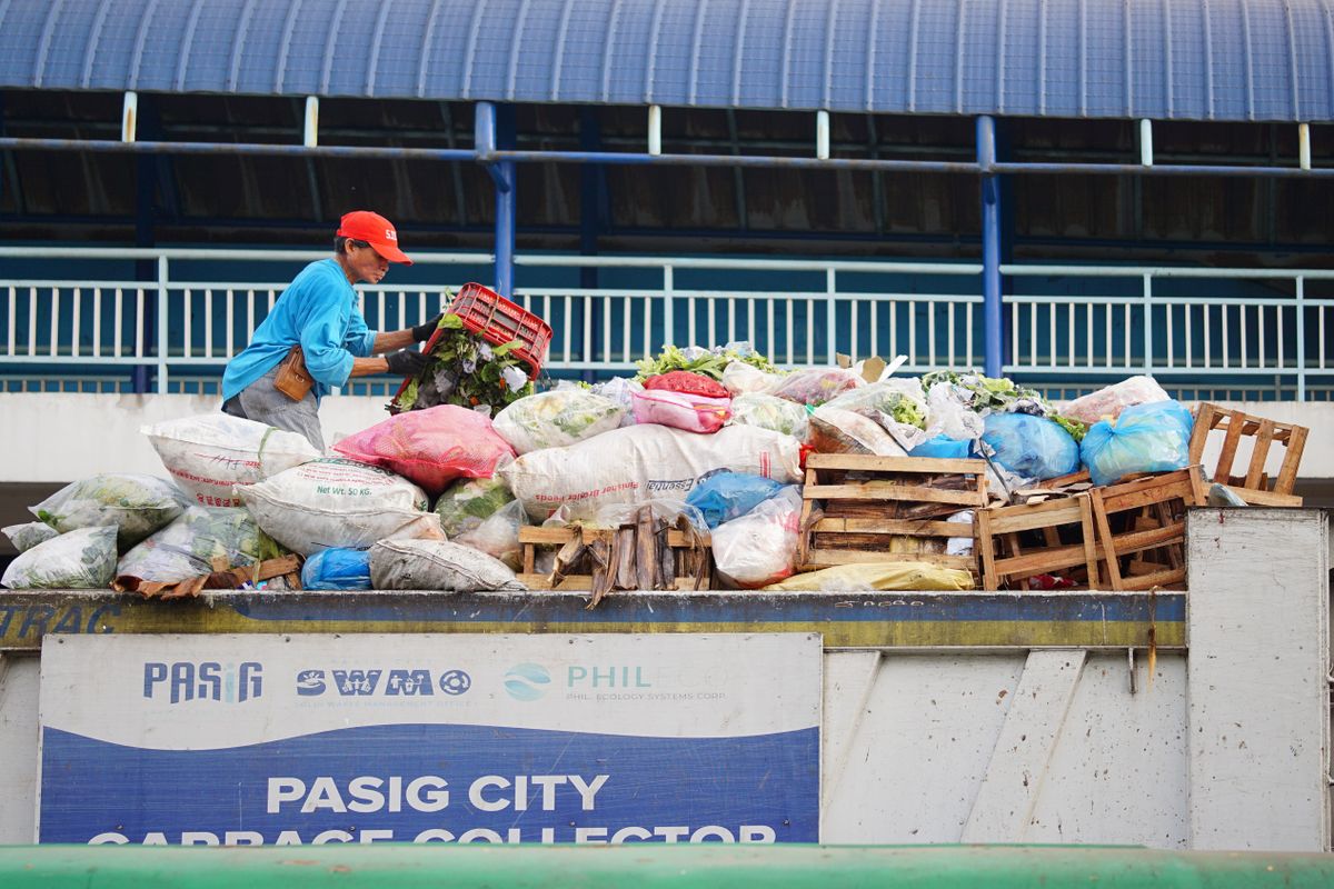 Seorang pekerja memilah dan menangani karung-karung sampah di atas truk pengangkut sampah, menggambarkan pekerjaan pemilahan sampah DLH