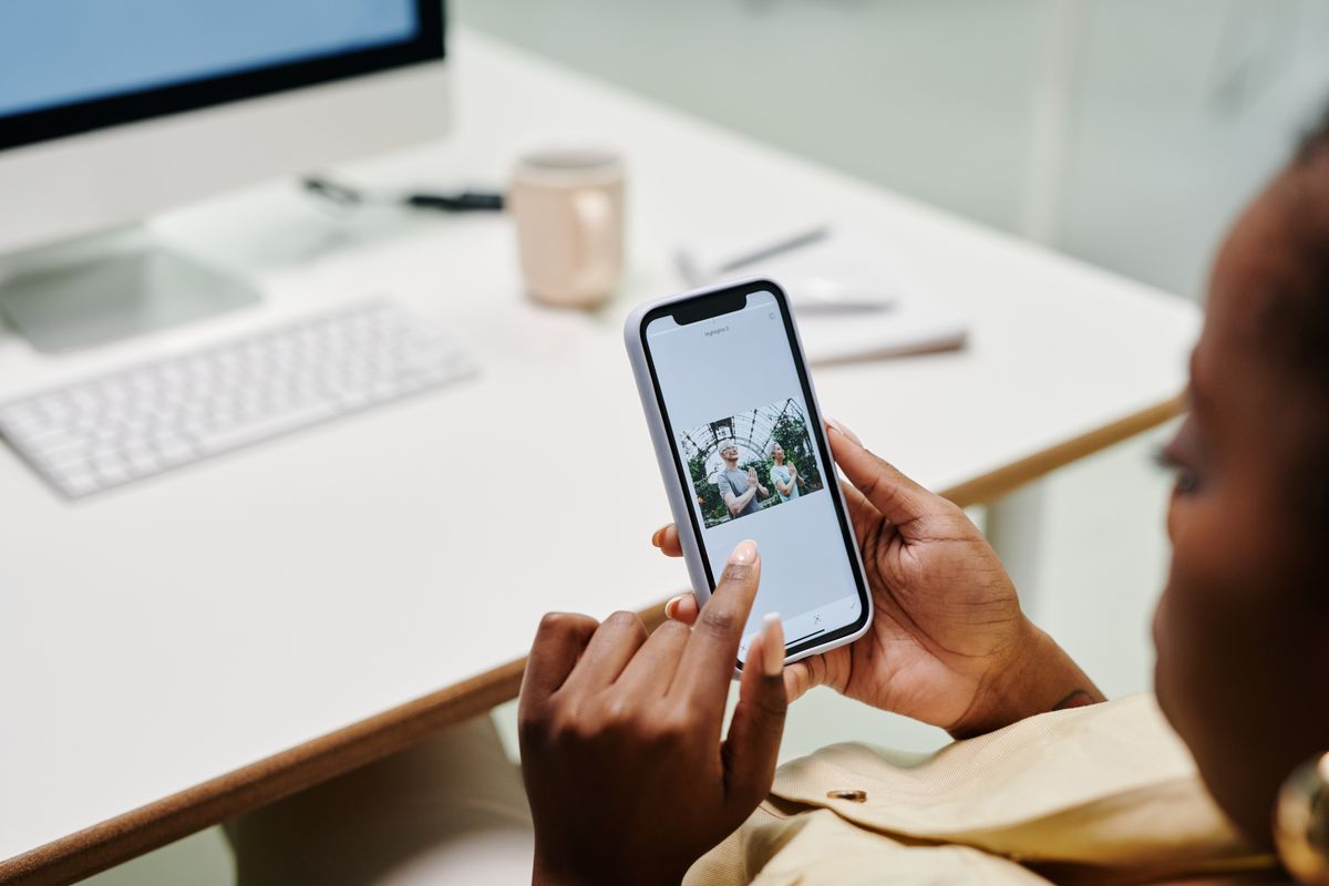 Tangan seseorang yang sedang mengoperasikan smartphone di dekat meja kerja, menggambarkan pendaftaran lowongan yang dilakukan secara online dari HP