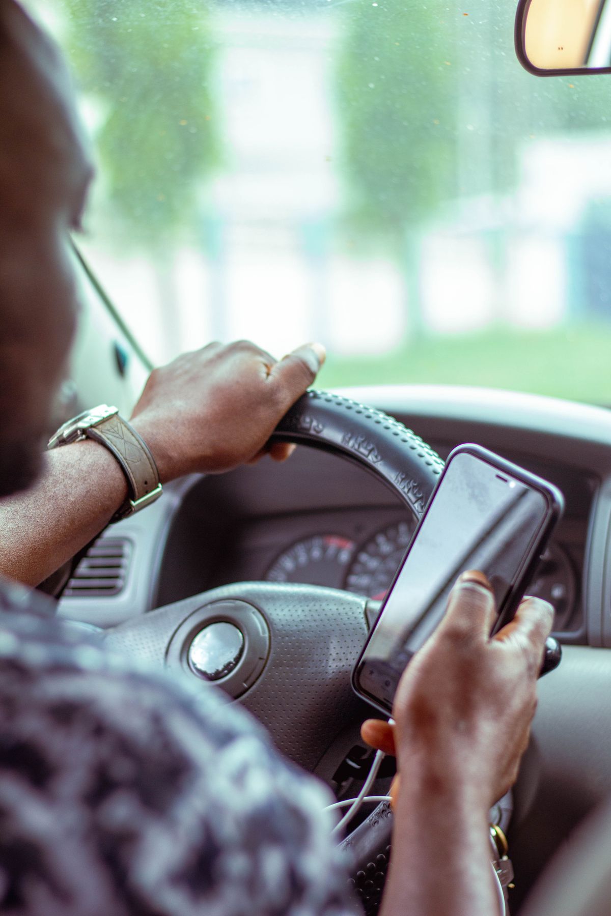 Pengemudi memegang HP sambil memegang setir mobil