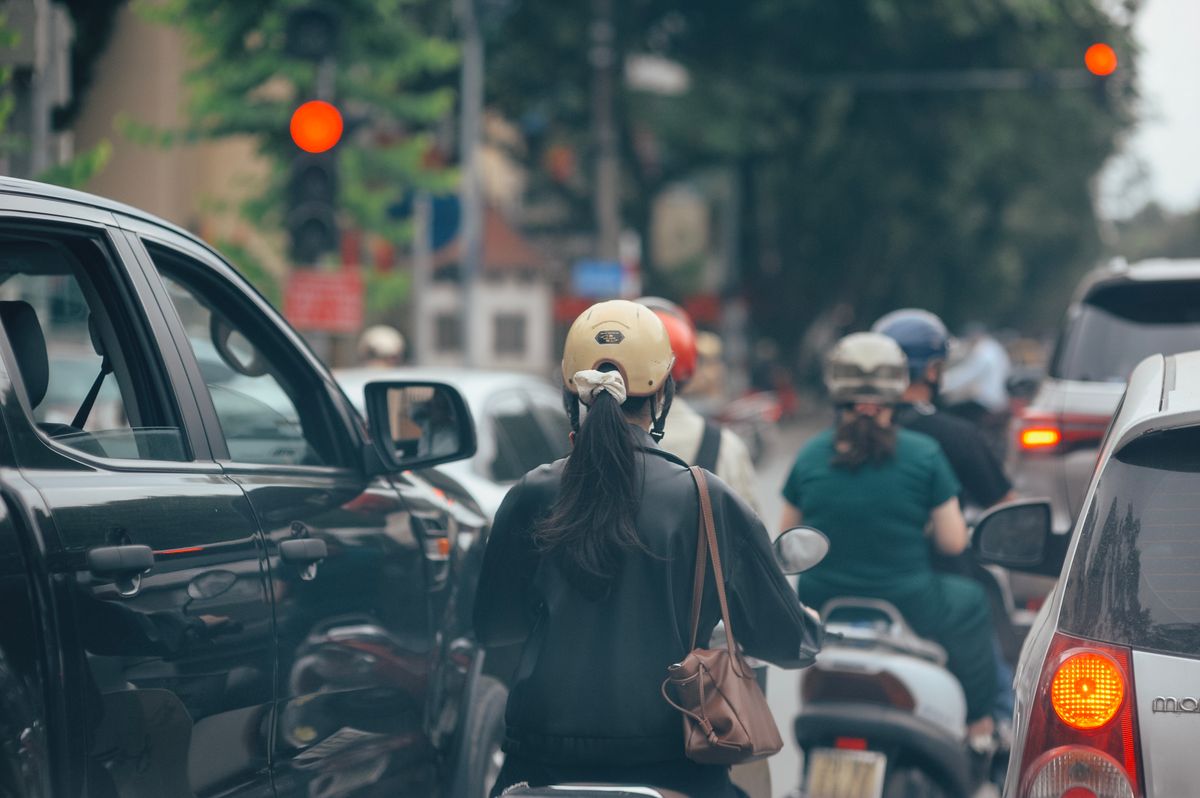 Pengendara motor berhelm menunggu lampu merah di jalan kota yang padat