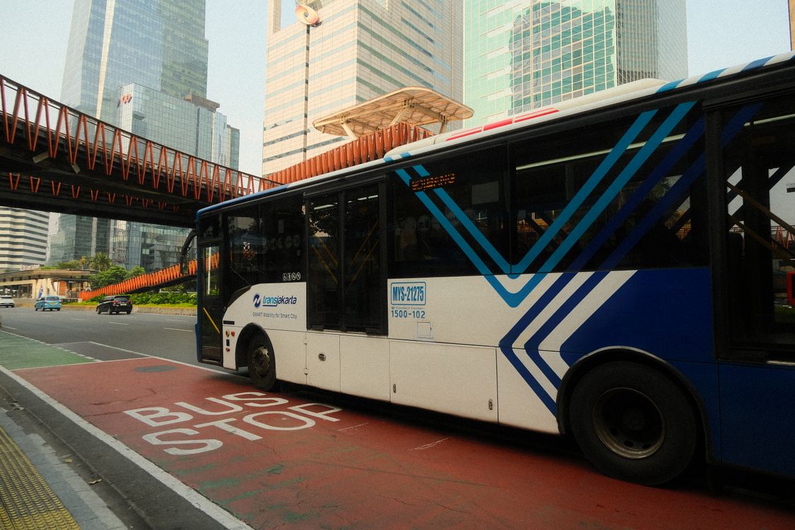 Bus TransJakarta berhenti di jalur bus stop dengan latar gedung pencakar langit Jakarta