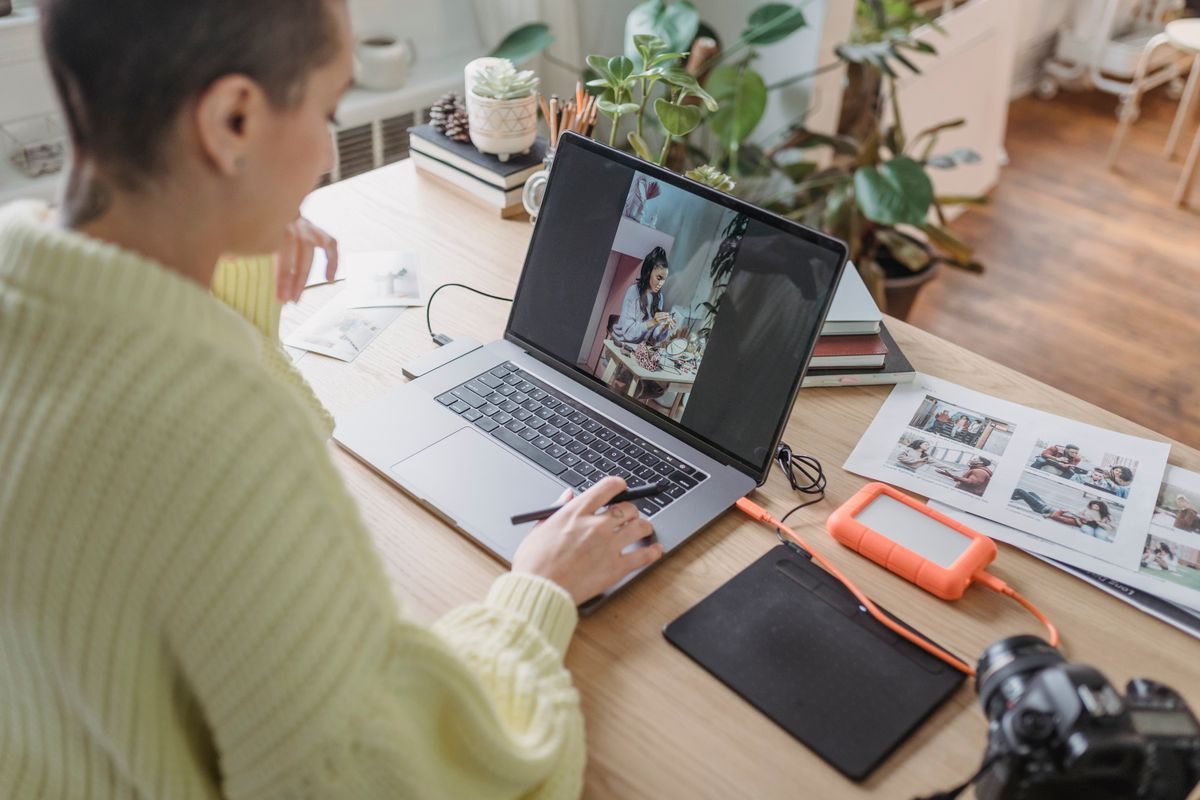Seorang perempuan mengedit foto di laptop dengan tablet gambar dan kamera di atas meja, menggambarkan aktivitas mengedit foto di komputer