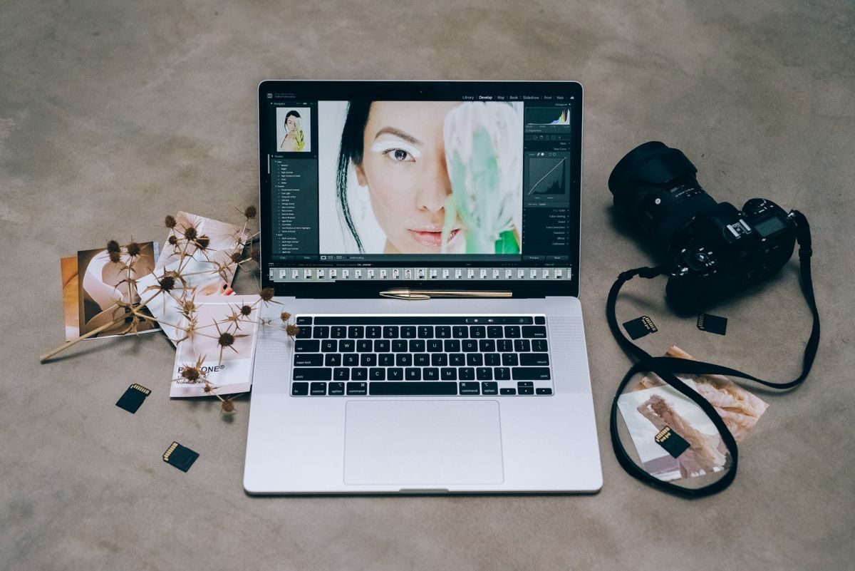 Laptop yang menampilkan foto potret sedang diedit, di samping kamera dan kartu memori di atas meja, menggambarkan retouch foto dari kamera